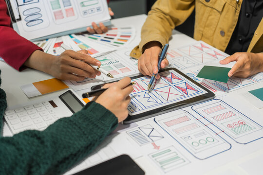 A group of people collaborates around a desk, discussing and reviewing user interface (UI) and user experience (UX) elements. usability, accessibility, and design principles for product development.