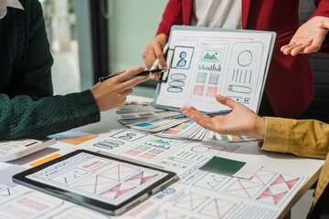 A group of people collaborates around a desk, discussing and reviewing user interface (UI) and user experience (UX) elements. usability, accessibility, and design principles for product development.