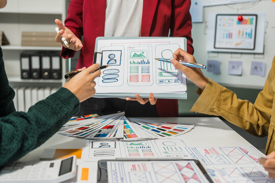 A group of people collaborates around a desk, discussing and reviewing user interface (UI) and user experience (UX) elements. usability, accessibility, and design principles for product development.