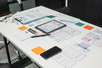 On a desk with paper, a tablet, and a laptop, a digital designer works on user interface (UI) and user experience (UX) concepts, focusing on usability, accessibility, and design principles.