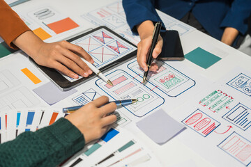 A group of people collaborates around a desk, discussing and reviewing user interface (UI) and user...