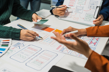 A group of people collaborates around a desk, discussing and reviewing user interface (UI) and user...