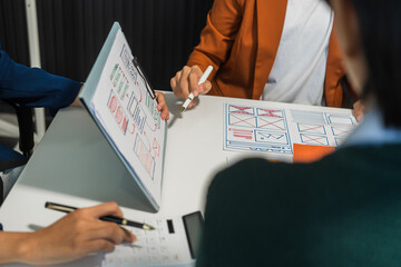 A group of people collaborates around a desk, discussing and reviewing user interface (UI) and user...