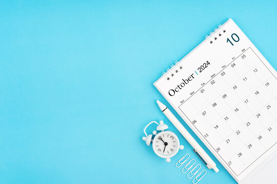 October 2024, Monthly desk calendar for 2024 year and alarm clock with paper clips on blue color background.