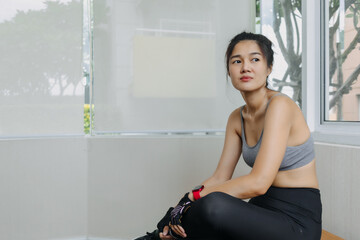 Asian Thai woman sitting on chair, relaxing and resting after done tired workout at gym, thinking something.