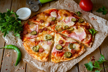 Italian pizza with smoked sausages, ham, fresh tomatoes, cucumbers and mozzarella on a wooden background. Pizza slices on a wooden background. Close-up.