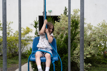 A little girl pulls a rope trying to lift herself in a chair. Concept of experimental children's education.