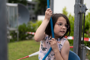 A little girl pulls a rope trying to lift herself in a chair. Concept of experimental children's education.