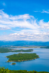 Obraz premium A serene lake nestled amidst towering mountains, with several islands, all beneath a cloud-filled sky