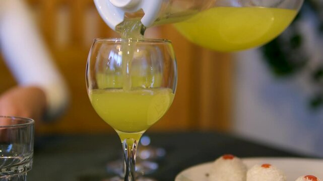 Pour orange juice Squeezing juice from half a tangerine to the glass by hand pressure, view on a background of other whole tangerines on a table