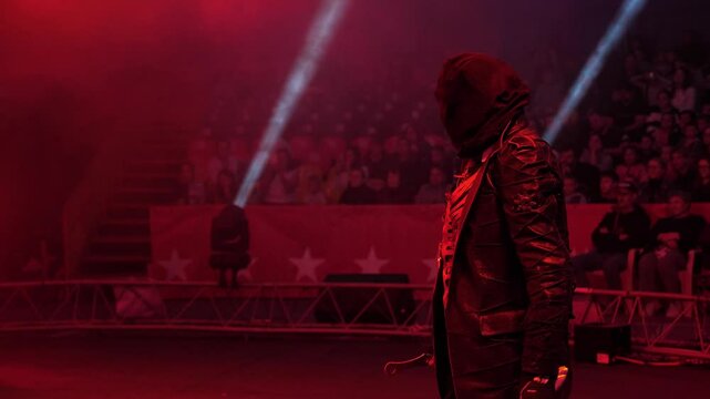 Portrait of a circus actor throwing knives, with a bag over his face, an actor with his eyes closed, throwing knives in the circus arena in the spotlight and smoke.