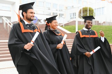 education, graduation and people concept - group of happy international students in mortar boards and bachelor gowns with diplomas