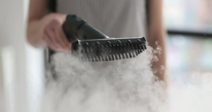 Woman holds cleaner brush with floating hot steam clouds in house. Female worker uses modern hygienic equipment. Housework technology