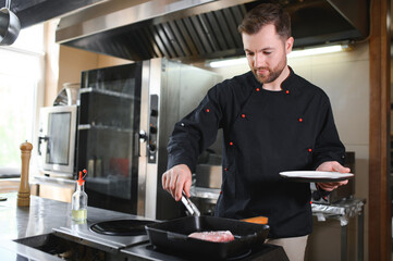 Chef in hotel or restaurant kitchen cooking, he is cutting meat or steak