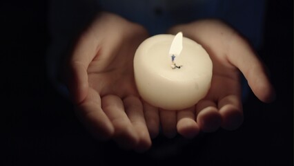 The sad girl holds a candle in hands in a dark room.
