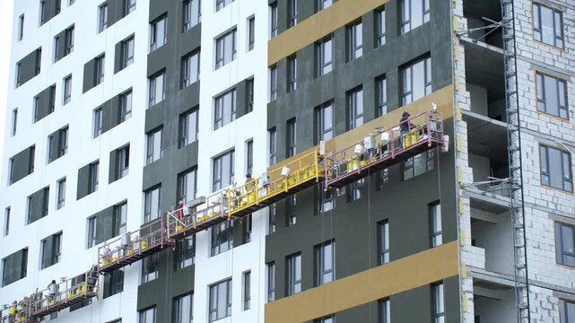 Workers securely stands on high lift near high-rise building. Employees add final touches to ultra-modern facade of newly constructed high-rise