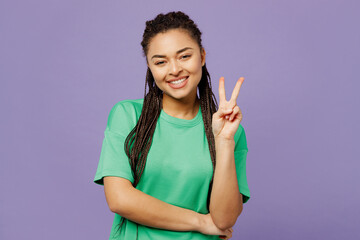 Young smiling happy woman of African American ethnicity with dreadlocks wear green t-shirt casual clothes looking camera show v-sign isolated on plain pastel light purple background Lifestyle concept