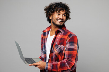 Young happy smiling Indian IT man wear red shirt casual clothes hold use work on laptop pc computer...