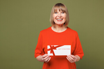 Elderly blonde woman 50s years old wear orange t-shirt casual clothes hold gift certificate coupon...