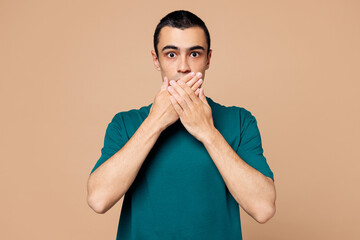 Young shocked surprised sad middle eastern man wears blue t-shirt casual clothes cover mouth with...