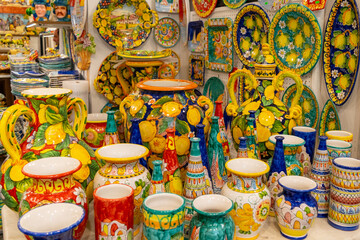 Colorful Italian ceramics from Amalfi region displayed in a shop. Brightly painted pottery including vases, plates, and bowls with lemon motifs. Traditional Italian craftsmanship and decorative art.