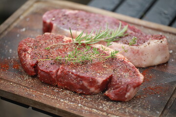 Seasoned raw steaks garnished with fresh thyme and rosemary on wooden board