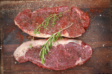 Seasoned raw steaks garnished with fresh thyme and rosemary on wooden board