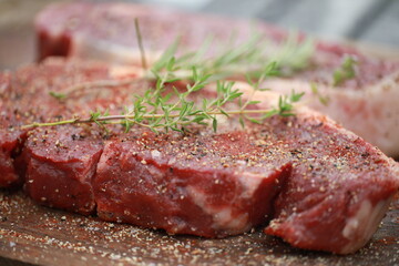 Seasoned raw steaks garnished with fresh thyme and rosemary on wooden board
