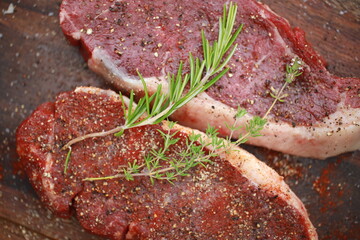 Seasoned raw steaks garnished with fresh thyme and rosemary on wooden board
