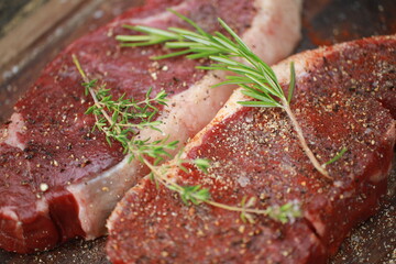Seasoned raw steaks garnished with fresh thyme and rosemary on wooden board