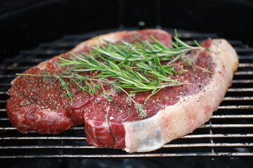 Seasoned raw steaks garnished with fresh thyme and rosemary on wooden board