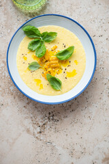 Sweet corn gazpacho in a blue and white plate, top view on a beige granite background, vertical shot with space