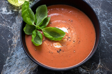Soup made of roasted tomatoes and red bell peppers, horizontal shot on a black marble background, middle close-up, selective focus