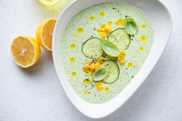 Chilled soup made of cucumber and topped with sweet corn, horizontal shot on a white stone surface, high angle view
