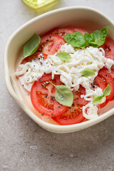 Beige serving tray with red tomato slices, stracciatella di bufala and basil, vertical shot, middle close-up, selective focus
