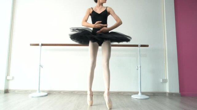 Young beautiful fourteen year old girl in black ballet tutu practicing ballet dancing practicing dancing as a black swan using bar pole, white wall in studio
