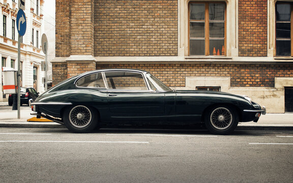 Green Jaguar E-type in front of old brick building. Side profile view of 1960s British sports car parked on a street. Vienna, Austria - July 30 2010.