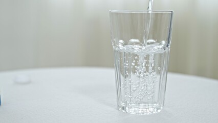 Pouring water from bottle into glass on white background
