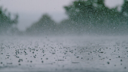 LOW ANGLE: Cinematic shot of hail falling on asphalt during a heavy rainstorm.