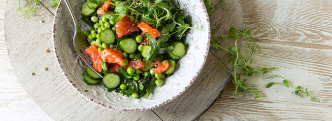 bowl of salad with red fish, cucumbers and green peas on the table