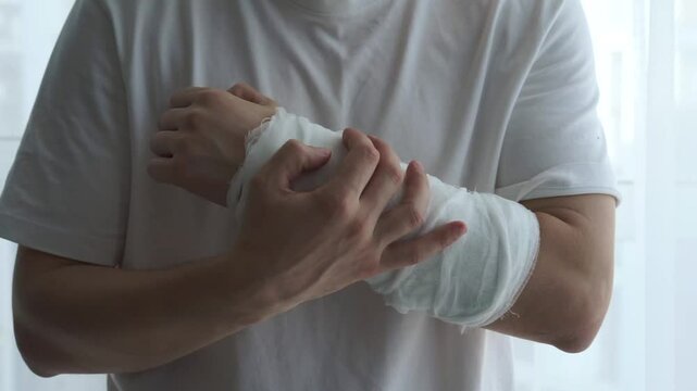 An unrecognizable man holds a broken arm with a cast with his healthy hand.
Pain in hand.
Discomfort from plaster