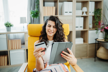 One young beautiful caucasian woman is buying online on her tablet using credit card from her home	