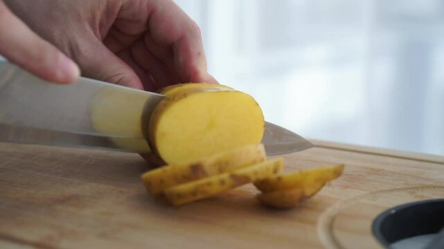 Hands with a knife cut potatoes on a wooden board in the kitchen. Healthy eating and lifestyle.