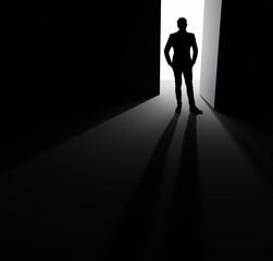 A man stands in the doorway of a large ajar door in the rays of light.