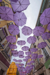 a village street with purple umbrellas hanging from the balconies for decoration and shade, in the artisan street market at the lavender festival, Brihuega, Guadalajara Spain, vertical