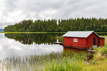Red wooden pier on lake shore with reflection of trees on shore
