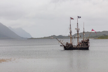 Wooden pirate ship in the middle of the sea with mountains in the background
