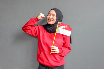 Beautiful Asian muslim woman saluting celebrating Indonesia's independence day on August 17 isolated on gray background