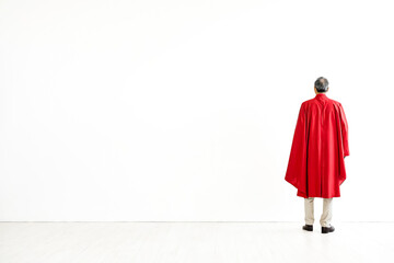 Senior Man in Red Cape Standing in Front of White Wall