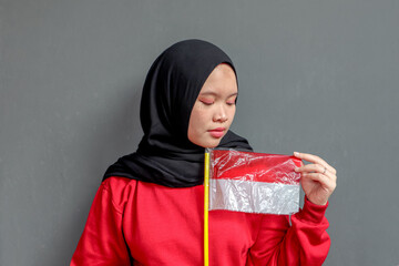 Beautiful Asian muslim woman saluting celebrating Indonesia's independence day on August 17 isolated on gray background